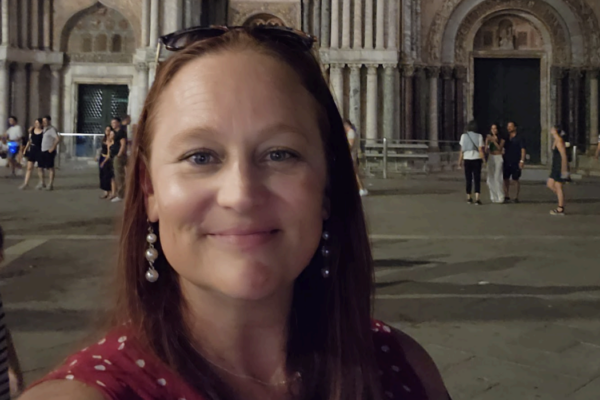 Smiling person taking a selfie in front of a historic building at night with ornate arches and columns.